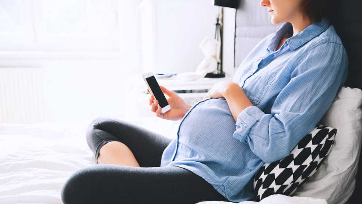 Mujer embarazada recostada mirando su telefono inteligente