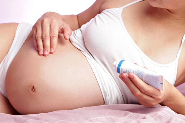 Mujer embaraza recostada untando crema en su cuerpo para prevenir la candidiasis