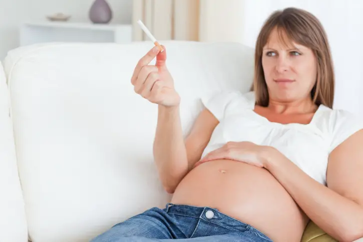 Mujer embarazada recostada observando con desprecio un cigarro