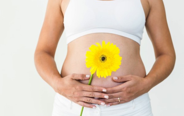 Mujer embarazada toncandose su panza descubierta con una flor